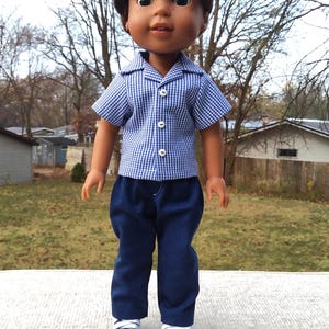 May include: A doll wearing a blue and white gingham shirt with a white collar, dark blue pants, and white sneakers.