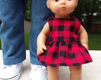 Puede incluir: Una muñeca con un vestido de cuadros rojos y negros. La muñeca está de pie junto a una muñeca más grande que lleva pantalones vaqueros azules y una camisa roja.