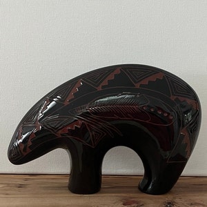 May include: Black ceramic bear figurine with red and black geometric designs. The bear is standing on all fours and has a stylized feather design on its back.