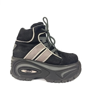 Puede incluir: Bota de plataforma negra con suela gruesa. La bota presenta una parte superior de ante negro con detalles grises y plateados, incluida una franja en el lateral. La suela es gruesa y tiene el texto "U.S.A.". La bota tiene cordones grises.