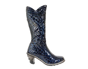 May include: A knee-high, dark blue boot with a glossy, textured finish. The boot has a unique heel design and a pointed toe. The boot's shaft has a distinctive, scalloped top edge. The boot is a stylish footwear item.