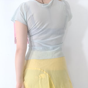 Puede incluir: Una blusa transparente azul claro con mangas cortas y cintura ce&ntilde;ida. La blusa se combina con una falda amarilla. La tela parece ligera y fluida, lo que sugiere una prenda de verano o primavera.