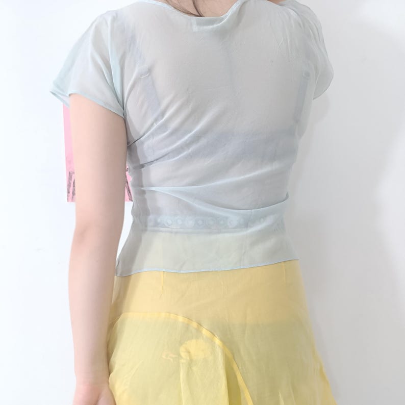 Puede incluir: Una blusa transparente azul claro con mangas cortas y cintura ce&ntilde;ida. La blusa se combina con una falda amarilla. La tela parece ligera y fluida, lo que sugiere una prenda de verano o primavera.
