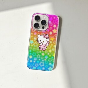 May include: A colorful phone case featuring a design of Hello Kitty. The case has a gradient background of pink, yellow, green, and blue with star patterns. Hello Kitty is wearing a pink dress and holding a small item.
