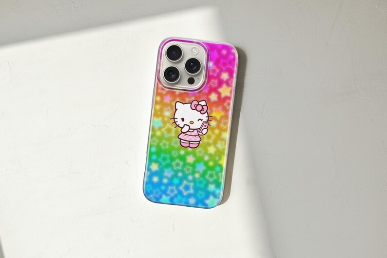 May include: A colorful phone case featuring a design of Hello Kitty. The case has a gradient background of pink, yellow, green, and blue with star patterns. Hello Kitty is wearing a pink dress and holding a small item.