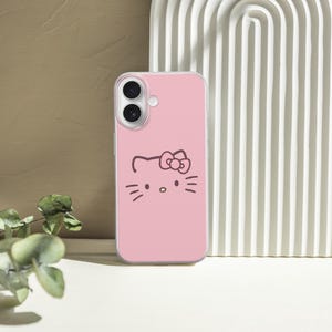 May include: Pink phone case featuring a black outline of a cat face with a bow. The phone case is set against a neutral background with a white arched structure and a sprig of greenery.