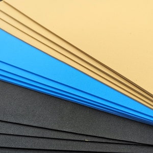 May include: Stack of foam sheets in black, blue, and tan colors. The sheets are arranged in a fan shape.