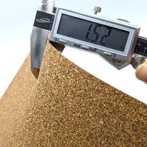 Puede incluir: Primer plano de una l&aacute;mina de corcho que se mide con un calibre digital. El calibre muestra 1,52 mm. La l&aacute;mina de corcho es de color marr&oacute;n natural con una textura rugosa.