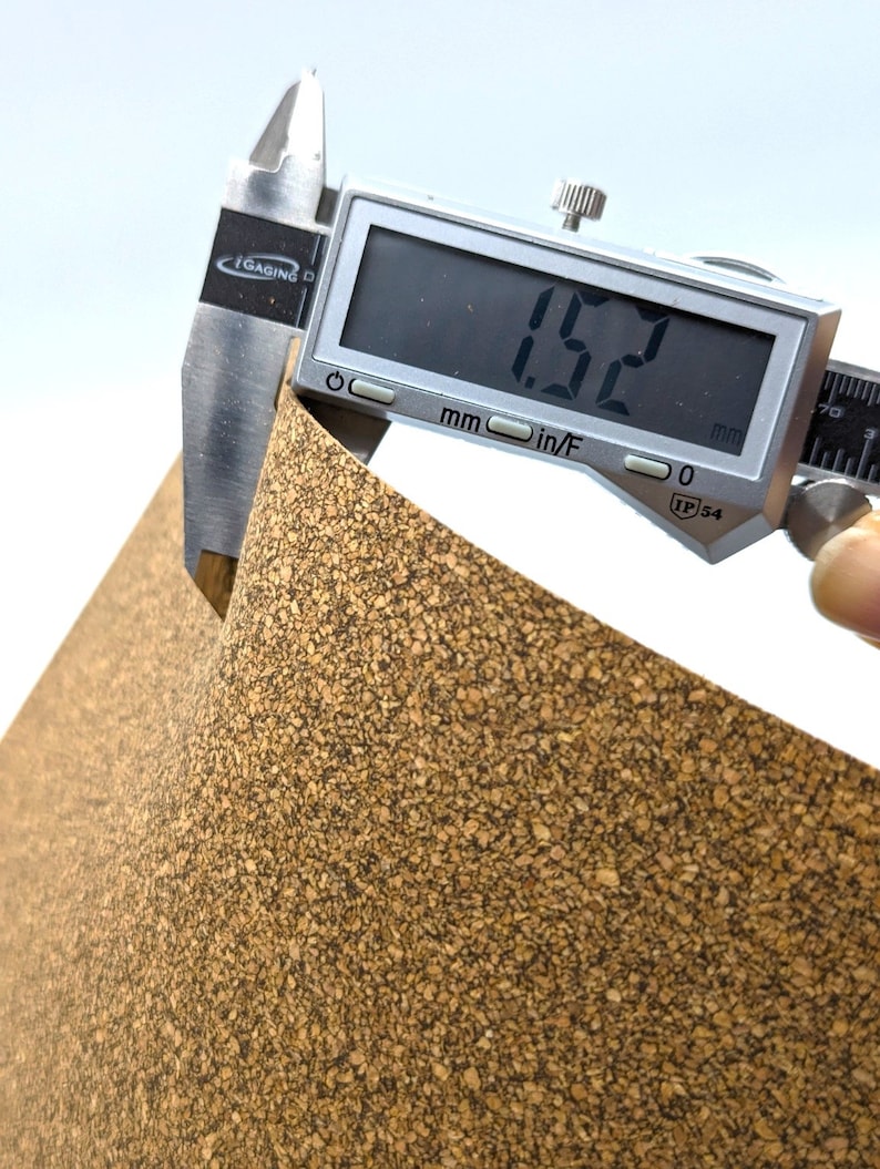 Puede incluir: Primer plano de una l&aacute;mina de corcho que se mide con un calibre digital. El calibre muestra 1,52 mm. La l&aacute;mina de corcho es de color marr&oacute;n natural con una textura rugosa.
