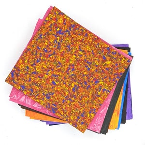 May include: A stack of colorful patterned paper sheets in various shades of pink, orange, purple, black, and blue. The top sheet features a swirling pattern of yellow, red, and blue.