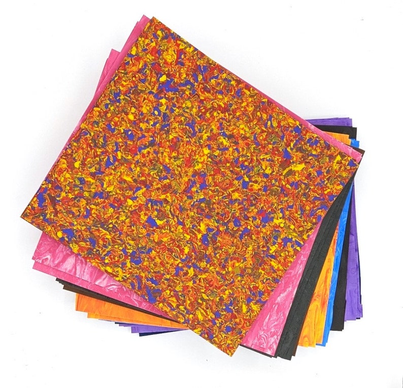 May include: A stack of colorful patterned paper sheets in various shades of pink, orange, purple, black, and blue. The top sheet features a swirling pattern of yellow, red, and blue.