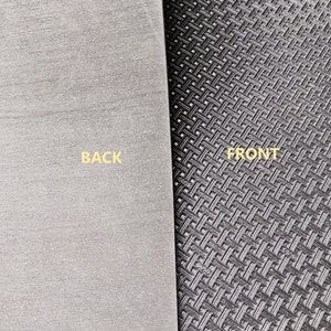 May include: A close-up of a black and grey mouse mat with a textured surface. The front side has a grid pattern, while the back side is smooth. The words "BACK" and "FRONT" are printed on the mat.