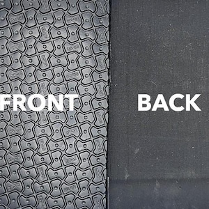 May include: Close-up of a black yoga mat with a textured surface. The front side of the mat has a pattern of small, raised squares. The back side of the mat is smooth. The words "FRONT" and "BACK" are printed on the mat.