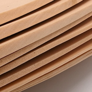 May include: A stack of beige leather sheets, each sheet is slightly curved, showing the texture of the leather.