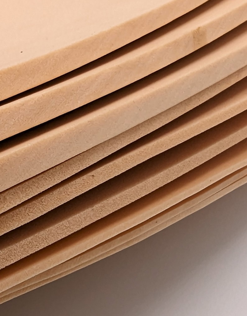May include: A stack of beige leather sheets, each sheet is slightly curved, showing the texture of the leather.
