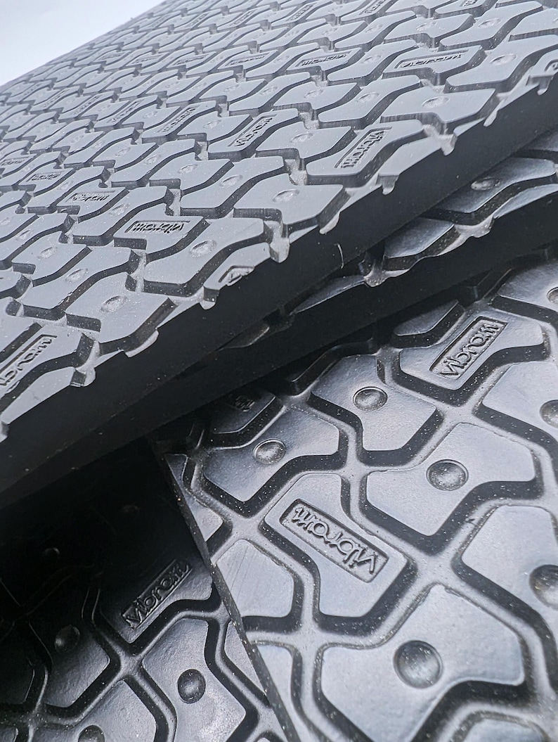 May include: Close-up of black rubber mats with a textured surface and the word "Vibram" embossed on the surface.