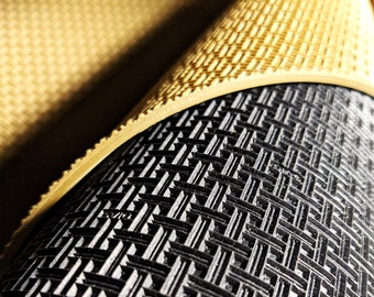May include: Close-up of a black and beige textured mat. The mat has a grid pattern and is rolled up.