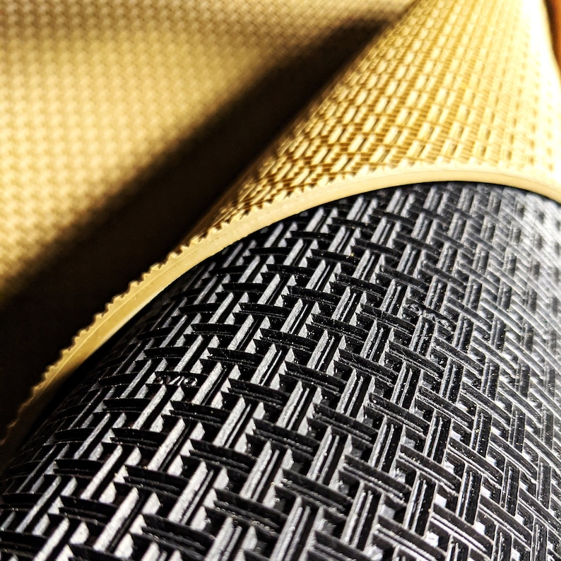 May include: Close-up of a black and beige textured mat. The mat has a grid pattern and is rolled up.
