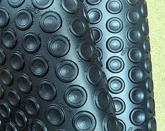 May include: Close-up of a black rubber sheet with a repeating pattern of raised, circular bumps. The material is flexible, with a portion of the sheet folded over, revealing the underside. The word "Vibram" is visible.