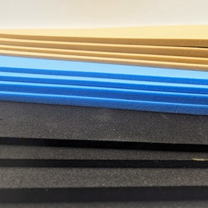 May include: A stack of foam sheets in various colors, including black, blue, and beige. The foam sheets are layered on top of each other.