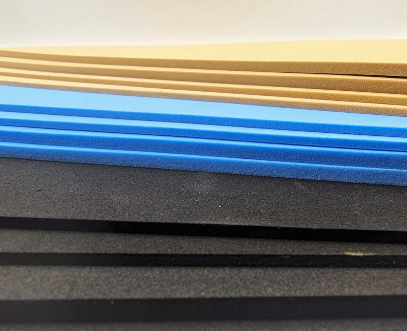May include: A stack of foam sheets in various colors, including black, blue, and beige. The foam sheets are layered on top of each other.
