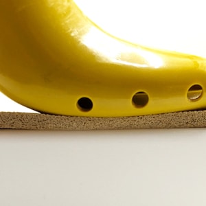 May include: A yellow shoe stretcher with holes on the bottom, resting on a brown foam surface.