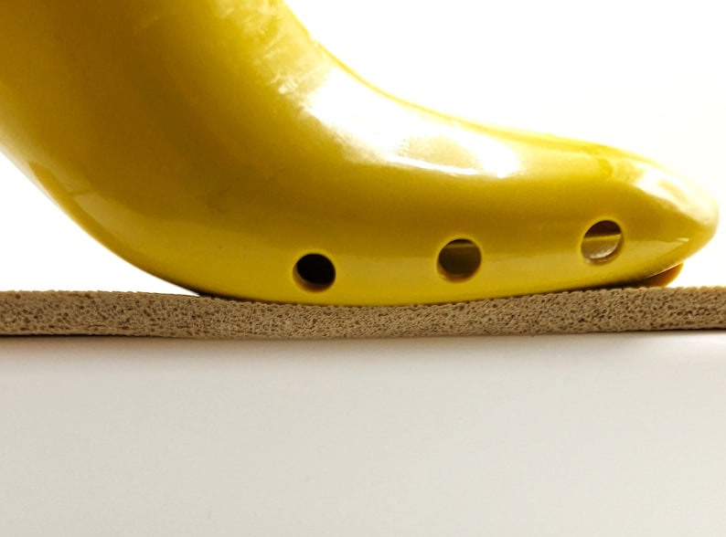 May include: A yellow shoe stretcher with holes on the bottom, resting on a brown foam surface.