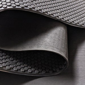 May include: Close-up of two black rubber mats with a textured hexagonal pattern. The mats are folded over each other, revealing the underside of the top mat.