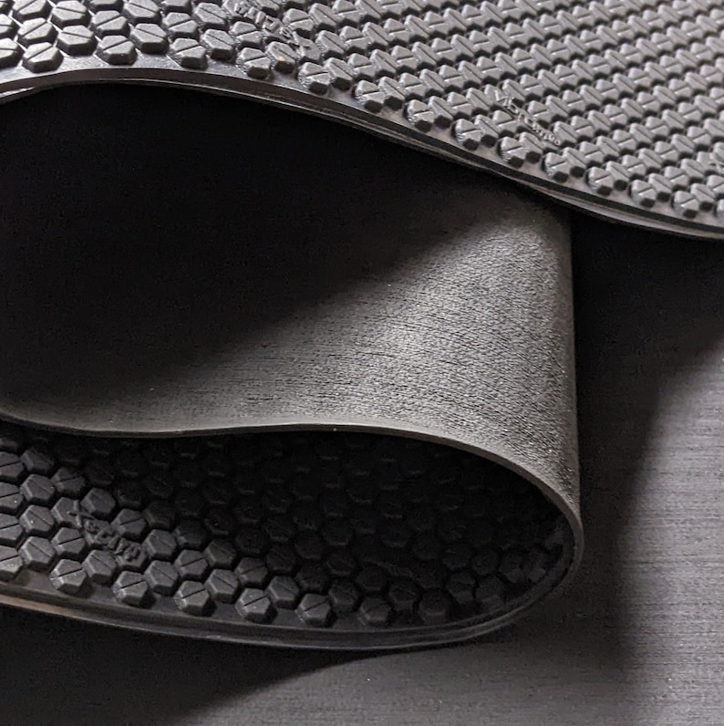 May include: Close-up of two black rubber mats with a textured hexagonal pattern. The mats are folded over each other, revealing the underside of the top mat.