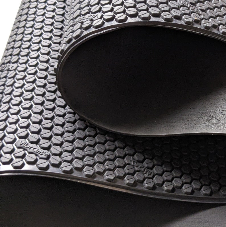 May include: Close-up of a black rubber exercise mat with a hexagonal pattern and the word "Vibram" printed on it.
