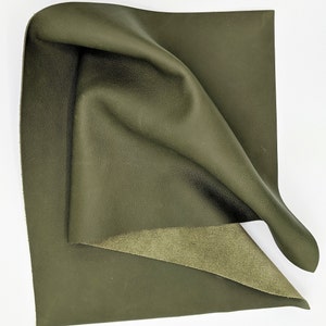 May include: A piece of dark green leather with a smooth, textured surface. The leather is folded in half, revealing a lighter green suede underside.