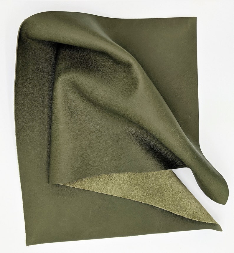 May include: A piece of dark green leather with a smooth, textured surface. The leather is folded in half, revealing a lighter green suede underside.