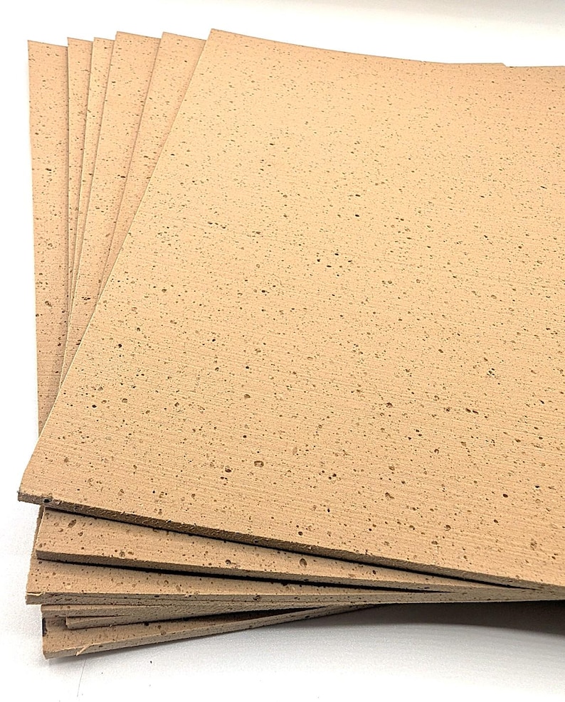May include: A stack of light brown cork sheets with a textured surface and small dark spots. The sheets are rectangular and appear to be new. The cork sheets are stacked on top of each other.