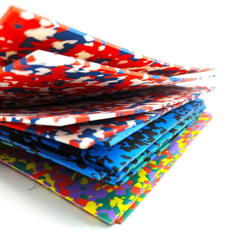 May include: A stack of colorful foam sheets with a camouflage pattern. The sheets are arranged in a staggered pattern, with the top sheet being red, white, and blue. The other sheets are blue, black, and purple.