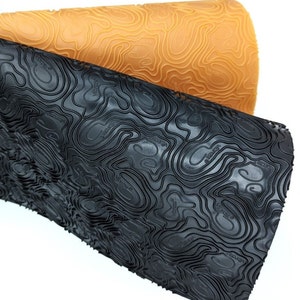 May include: Two rolls of textured rubber material. One roll is black, the other is tan. Both rolls have a topographic map pattern embossed on the surface. The rubber material is likely used for shoe soles or other outdoor gear.