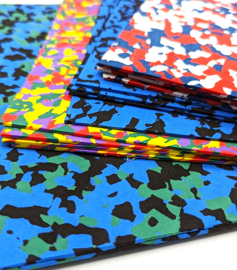 May include: A stack of colorful foam sheets with a camouflage pattern. The sheets are in various colors, including blue, green, red, yellow, and purple. The sheets are stacked on top of each other, and the top sheet is blue with black and green camouflage.