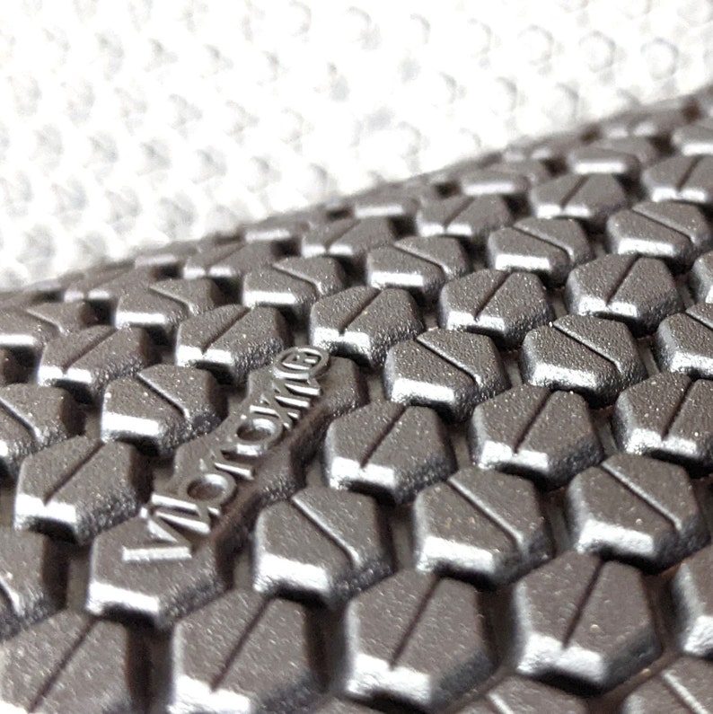 May include: Close-up of a black textured surface with a hexagonal pattern. The word "Vibram" is embossed in the surface.