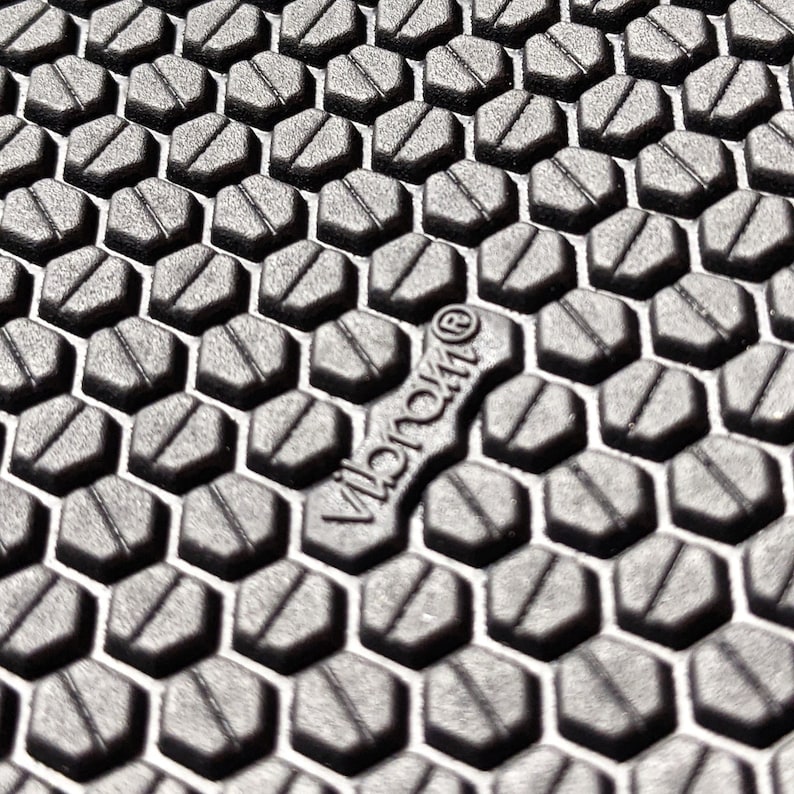 May include: Close-up of a black textured surface with a hexagonal pattern. The text "Vibram&reg;" is visible in the center of the image.