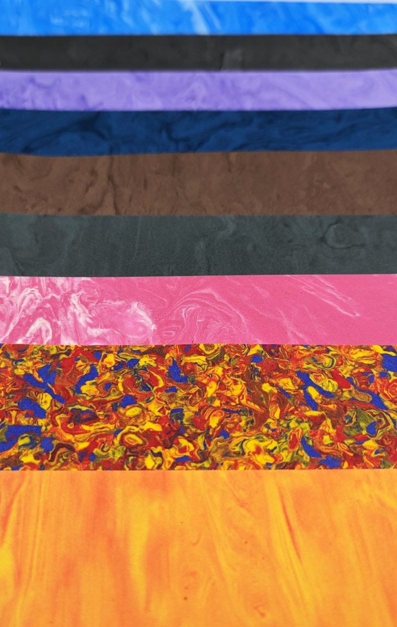 May include: A stack of colorful, marbled, and textured sheets of paper. The colors include blue, black, purple, brown, gray, pink, red, yellow, and orange.