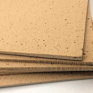 May include: A stack of four rectangular cork boards. The boards are a light brown color with a textured surface and small dark spots. The edges of the boards are rough and show the layered construction of the material.