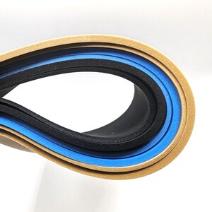May include: Close-up of three layers of foam material rolled into a circle. The outer layer is a light brown color, the middle layer is blue, and the inner layer is black.