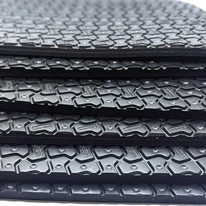 May include: Close-up of a stack of black rubber sheets with a textured surface. The sheets have a repeating pattern of small, raised squares.