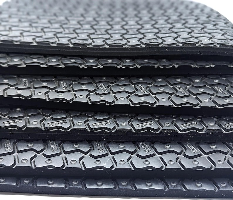 May include: Close-up of a stack of black rubber sheets with a textured surface. The sheets have a repeating pattern of small, raised squares.