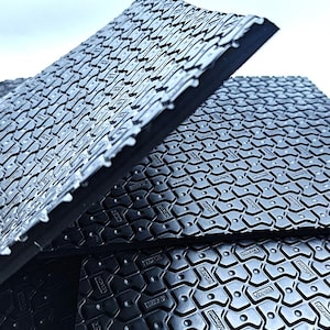 May include: Close-up of black rubber floor tiles with a textured surface and the word "Vibracoustic" embossed on each tile.