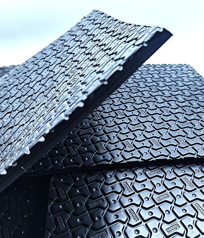May include: Close-up of black rubber floor tiles with a textured surface and the word "Vibracoustic" embossed on each tile.