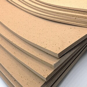 May include: A stack of light brown foam sheets with a textured surface. The sheets are rectangular with rounded corners and appear to be layered. The foam has a porous appearance.