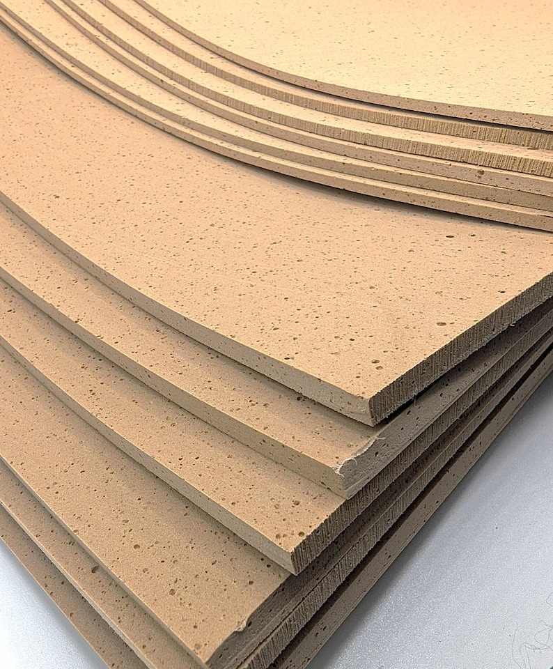 May include: A stack of light brown foam sheets with a textured surface. The sheets are rectangular with rounded corners and appear to be layered. The foam has a porous appearance.