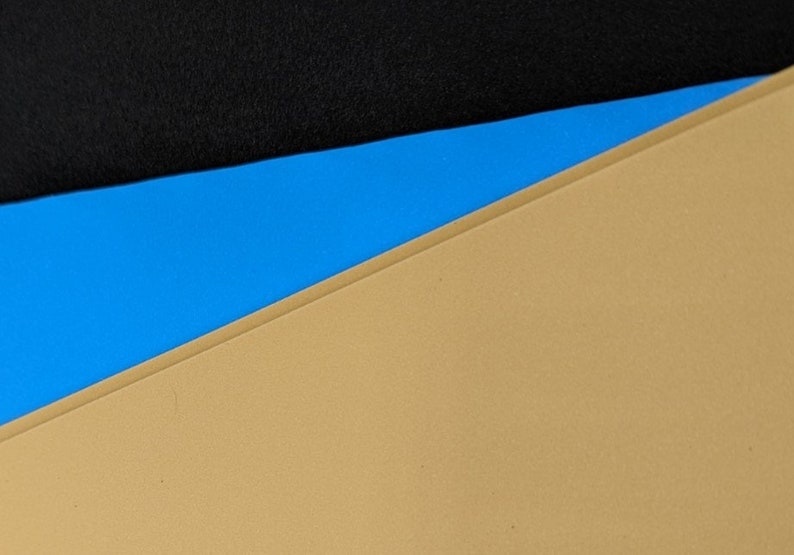 May include: A close-up of a tri-color background with a black top layer, a blue middle layer, and a tan bottom layer.