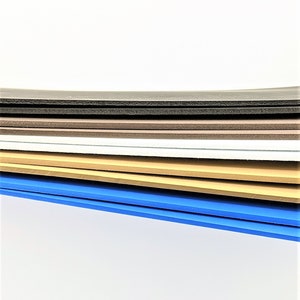 Pode incluir: Uma pilha de folhas de espuma em v&aacute;rias cores, incluindo preto, marrom, branco, bege e azul. As folhas est&atilde;o dispostas em um padr&atilde;o escalonado, com a folha azul na parte inferior.