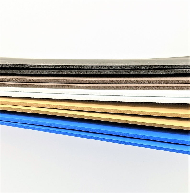 Pode incluir: Uma pilha de folhas de espuma em v&aacute;rias cores, incluindo preto, marrom, branco, bege e azul. As folhas est&atilde;o dispostas em um padr&atilde;o escalonado, com a folha azul na parte inferior.